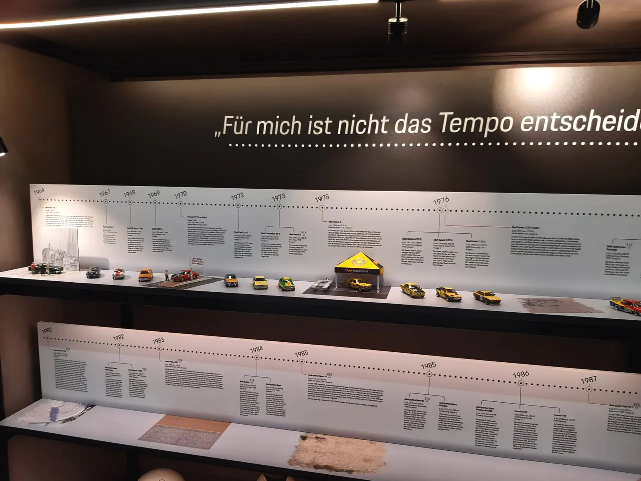 Vitrine mit Zeitleiste und Modellfahrzeugen unter einem Zitat von Walter Röhrl