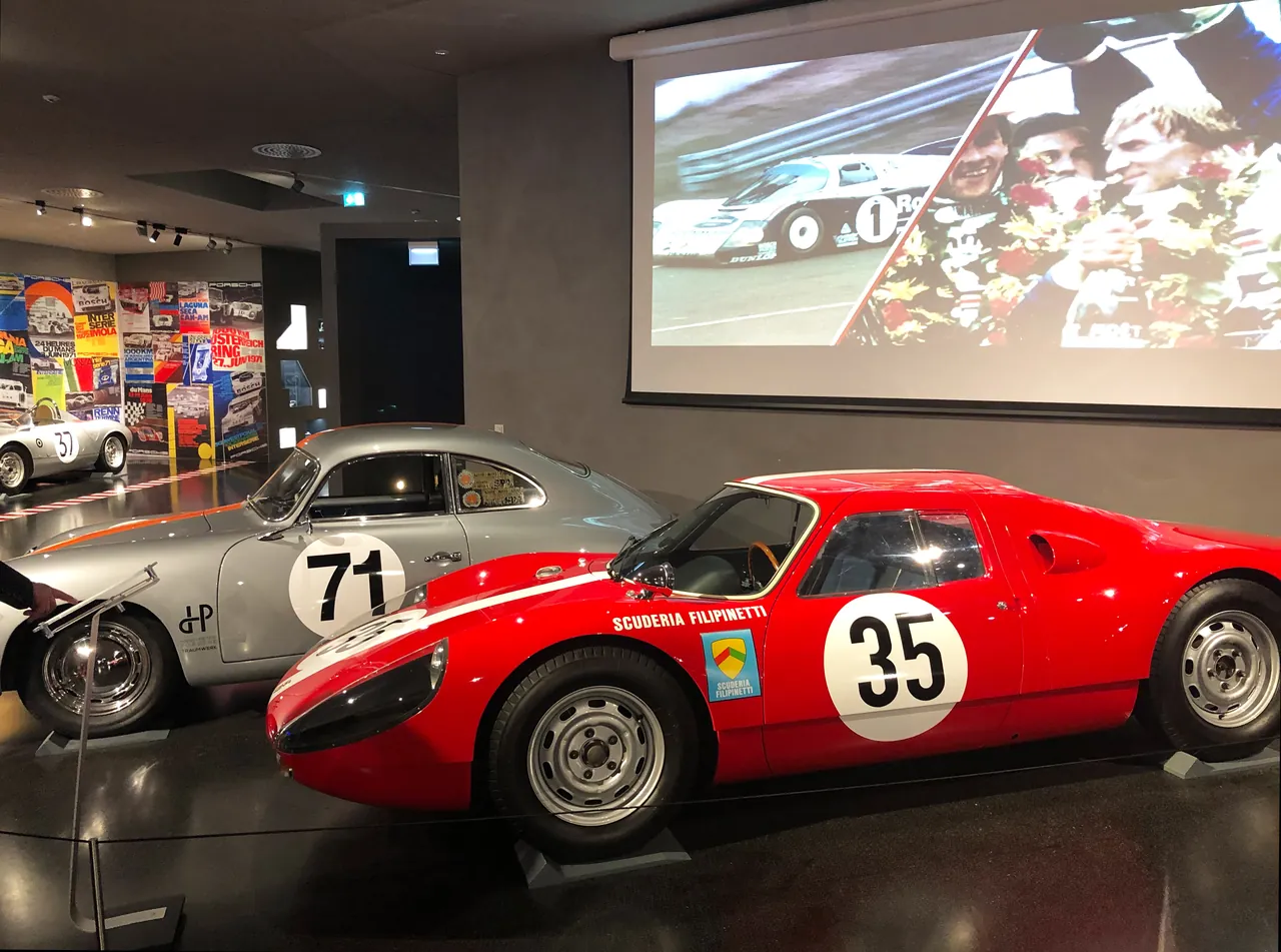 Originalfahrzeuge Porsche 904 in Silber und Rot vor einer Videowand